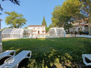 A backyard with a swimming pool, covered seating, and a house in the background.