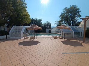 Ein Poolbereich mit gefliestem Boden, Sonnenschirmen und Glasverkleidungen.
