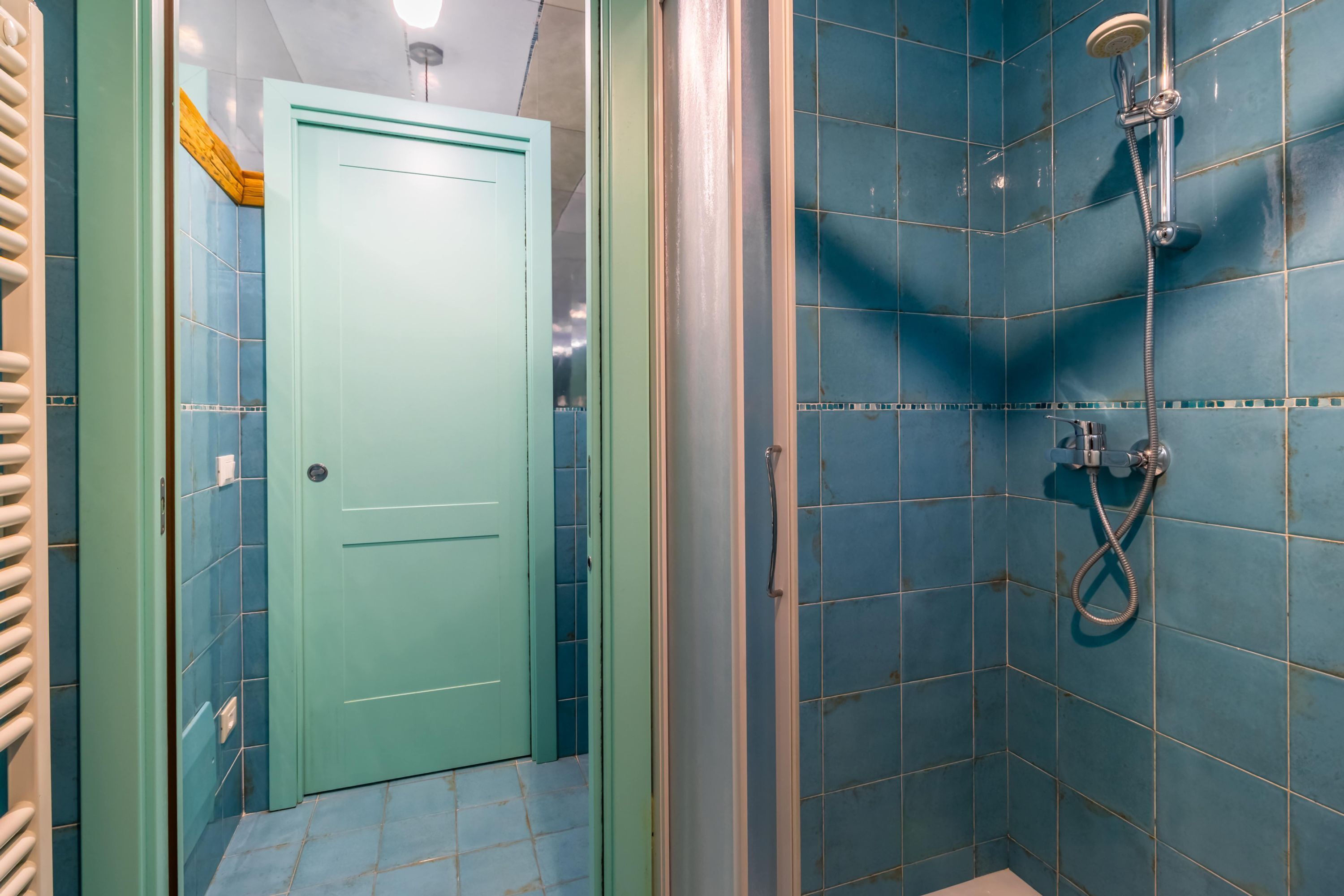 A bathroom with blue tiles, a shower, and a green door.