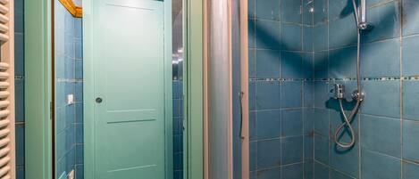 A bathroom with blue tiles, a shower, and a green door.