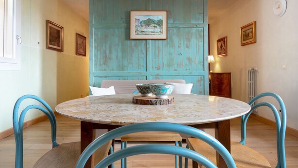 A dining area with a round table, blue chairs, and a teal wall with framed pictures. - Borgo al Sole 2 by Wonderful Italy (Puegnago del Garda)
