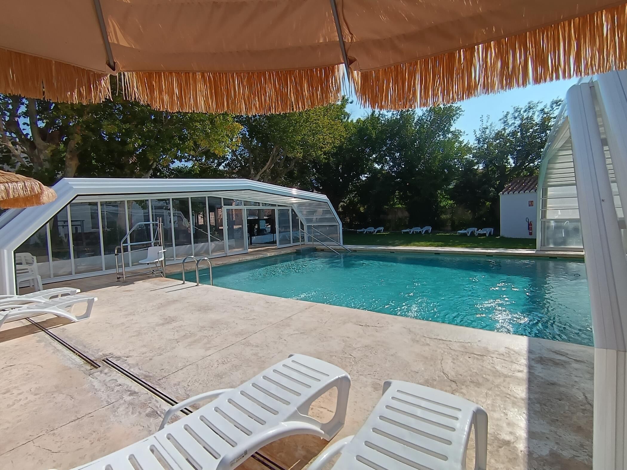 Una piscina amb zona coberta, gandules i vista despejada als arbres circumdants.