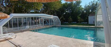 Una piscina amb zona coberta, gandules i vista despejada als arbres circumdants.