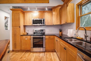 A kitchen with wooden cabinets, stainless steel appliances, a black countertop, and a window.