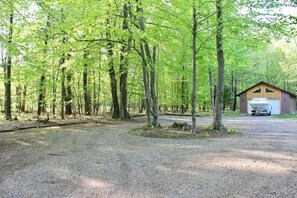 A gravel parking area with a single-story building, a covered boat storage area, and a forested backdrop.