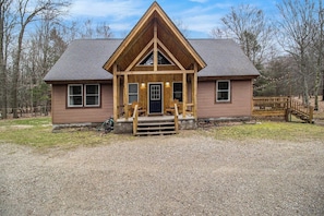 A wooden cabin with a gabled roof, a front porch, and a gravel driveway.