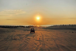A desert landscape with a vehicle on a sandy path leading towards a sunset.