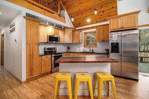 Une cuisine avec des meubles de rangement en bois, un réfrigérateur en acier inoxydable et un îlot central en bois avec des tabourets.