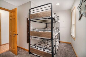 A bunk bed with a wooden headboard in a room with carpeted flooring and a wooden door.