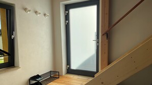 Un escalier étroit doté d’une rampe en bois, une petite table en bois avec un porte-chaussures, et une porte avec un panneau en verre dépoli.