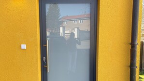 Un bâtiment jaune avec une porte sombre, un paillasson et un petit luminaire extérieur.