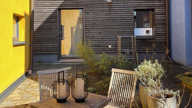Une maison en bois avec un toit en tuiles, une fenêtre et un petit espace extérieur aménagé avec une table et des chaises.