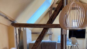 Une pièce avec un plafond en pente, des poutres en bois, un luminaire suspendu et deux chaises blanches.