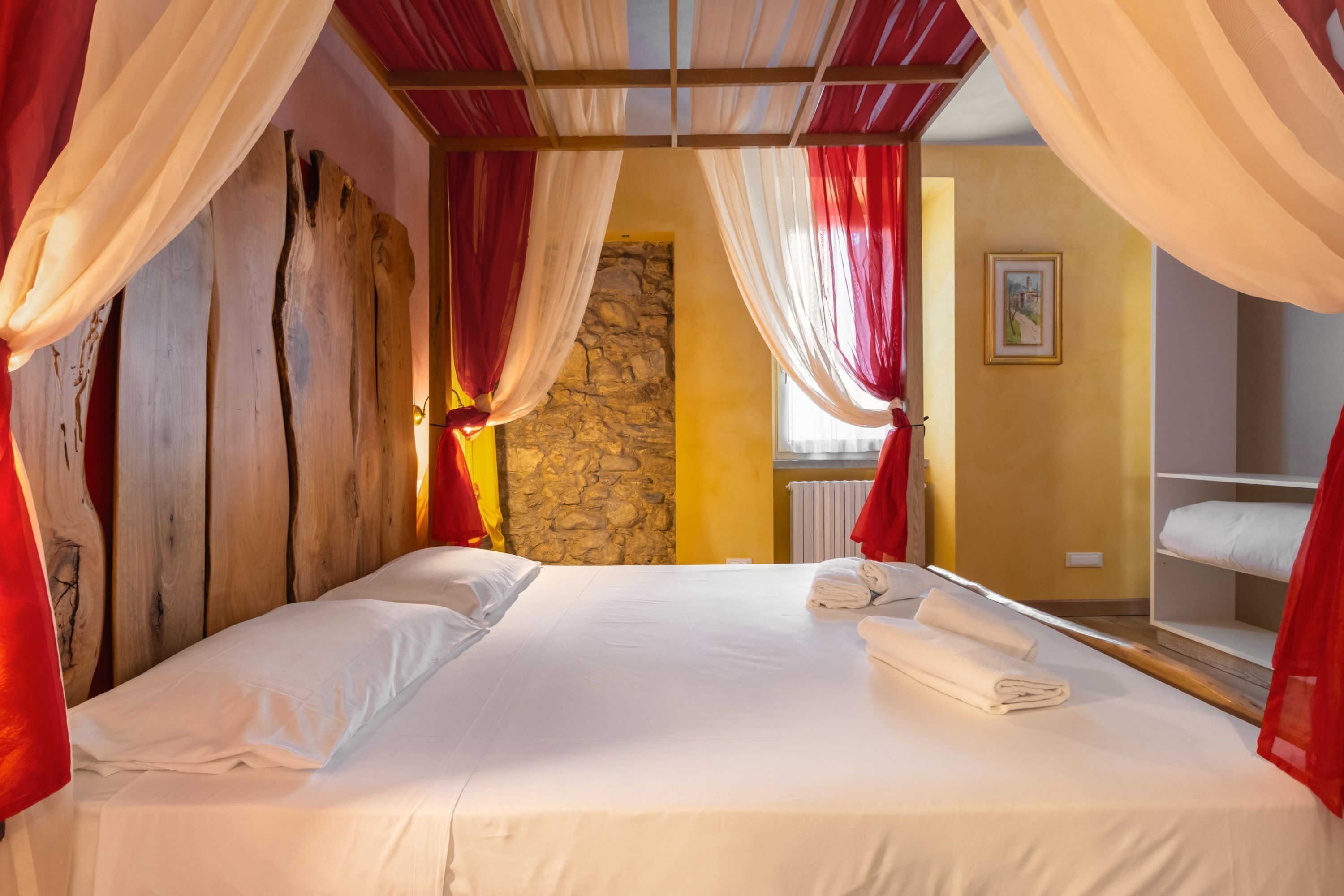 A bed with white linens, red curtains, and a stone wall in the background.