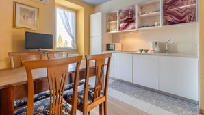 Eine moderne Küche mit weißen Schränken, einem Esstisch mit Holzstühlen und einem Fernseher an der Wand.