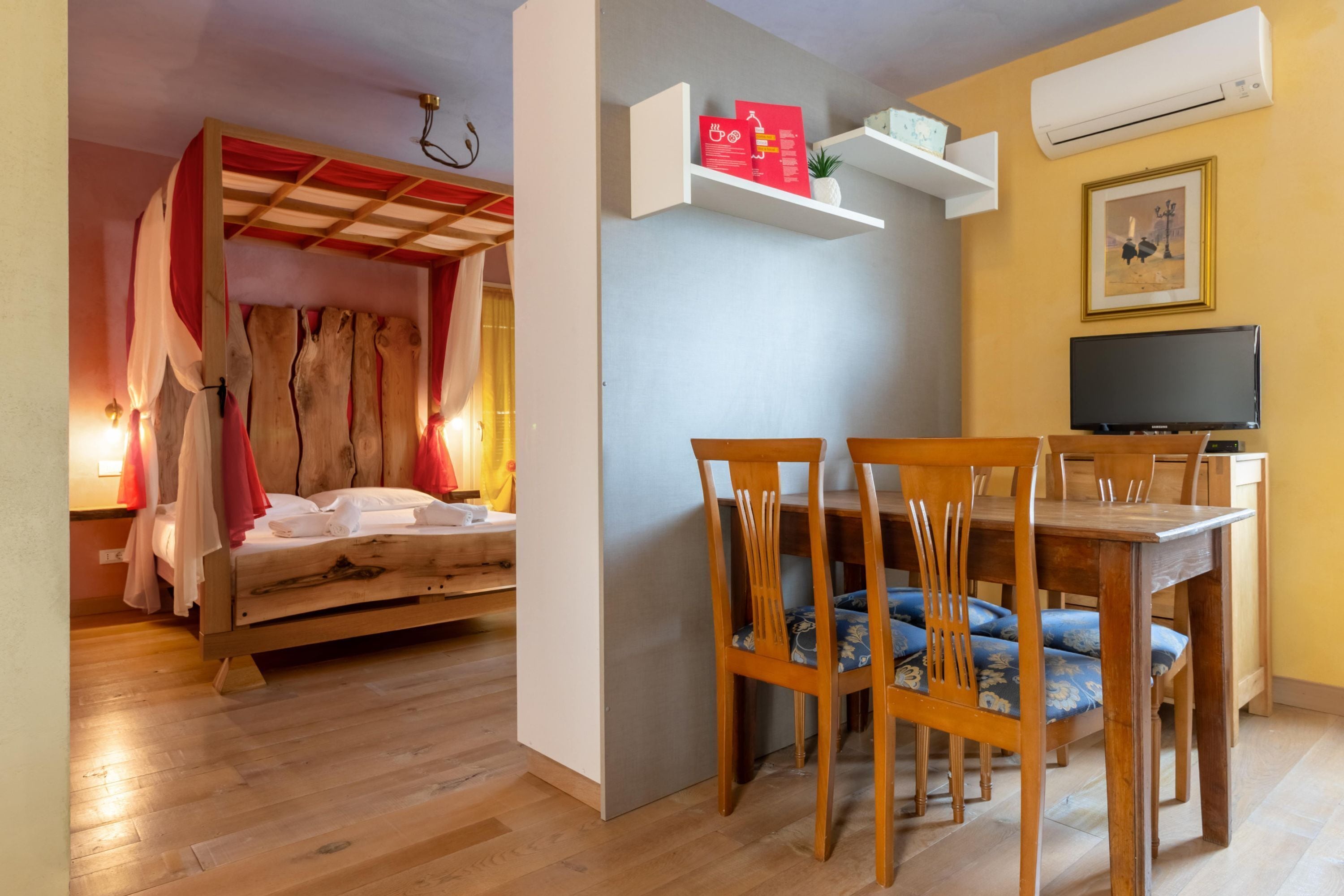 Une pièce comprenant un lit en bois, une table à manger avec des chaises, un téléviseur et une étagère avec divers objets.
