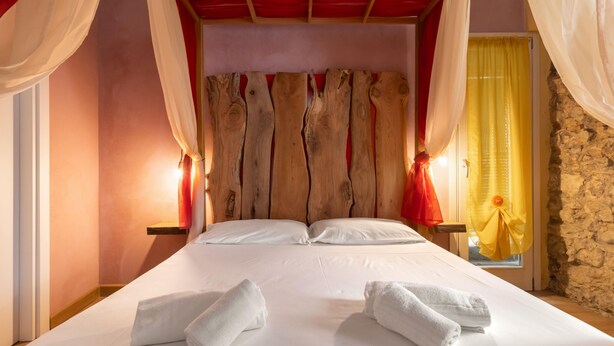Ein großes Bett mit weißen Leinen und zwei Handtüchern, ein Holzkopfstück und eine Steinwand.