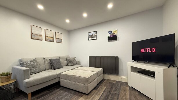A modern living room with a sectional sofa, a flat-screen TV, and a white entertainment unit. - The Market Hideaway - Bedale town centre (Bedale)