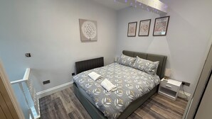 A modern bedroom with a large bed, a nightstand, a wall-mounted shelf, and a ceiling light fixture. - The Market Hideaway - Bedale town centre (Bedale)