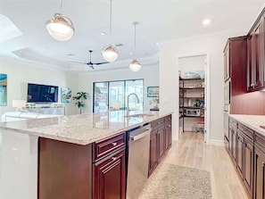 Una cocina moderna con una isla central, iluminación colgante y vistas al salón.