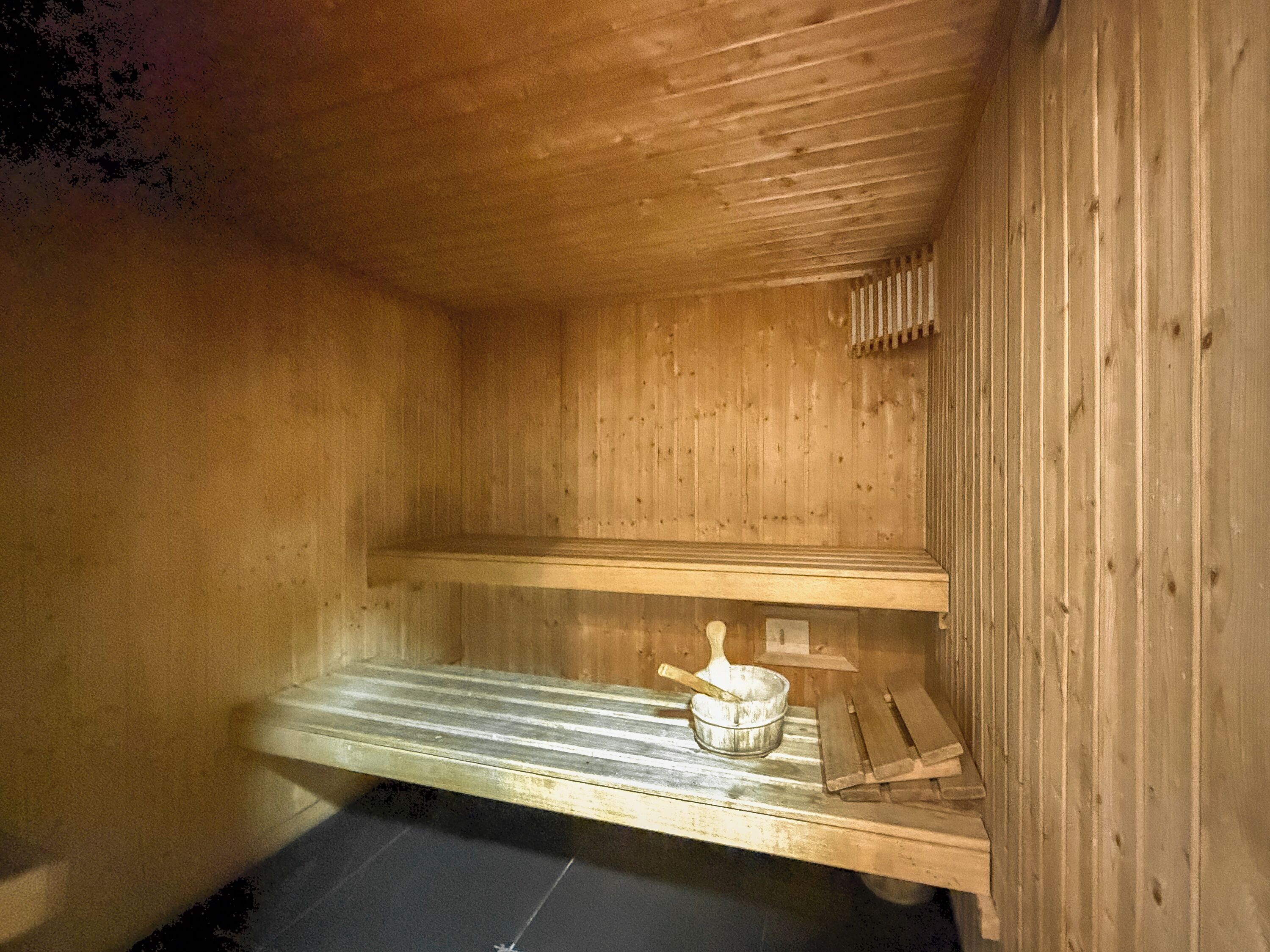 A wooden sauna with benches and a bucket.