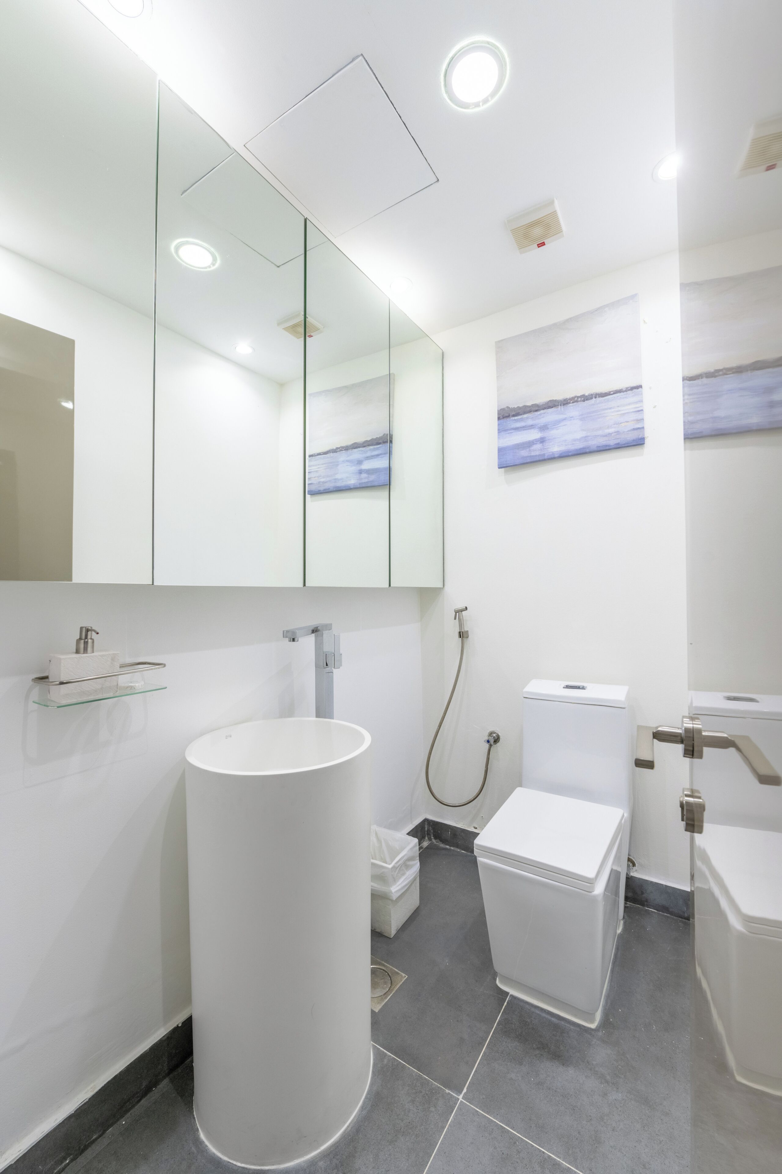 A modern bathroom with a large mirror, a round sink, a toilet, and a shower.