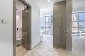 A modern hotel room with a large window, a walk-in closet, and a bathroom with a bathtub and sink. - Waterfront 3BR with Marina View at DEC (Dubai)