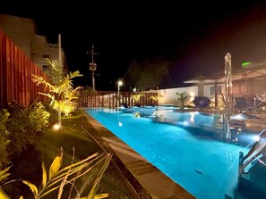 A nighttime swimming pool with a red fence, palm trees, and lounge chairs. - Maré Alta by AFT (Tamandaré)