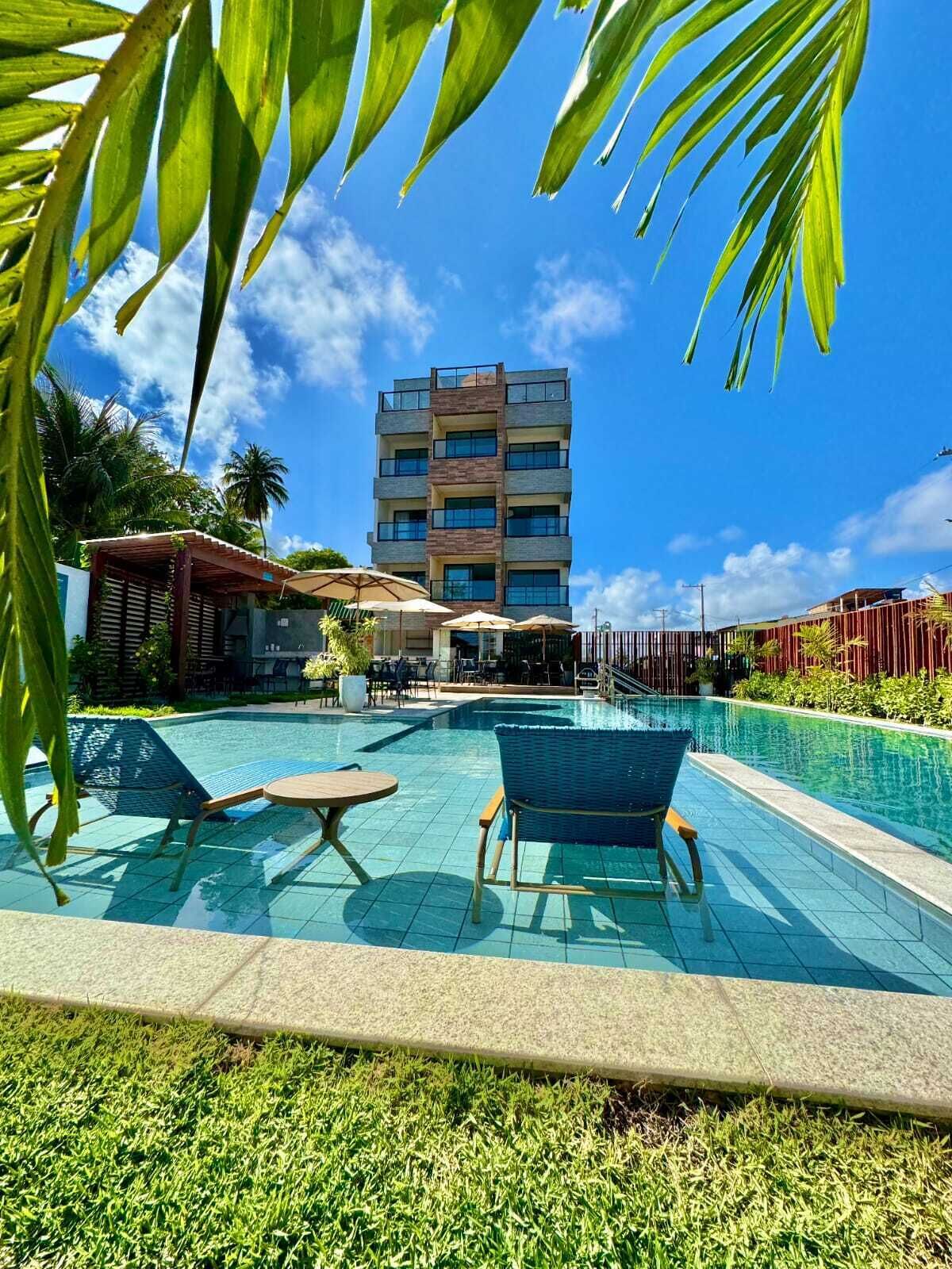A swimming pool with lounge chairs, a building in the background, and palm trees.