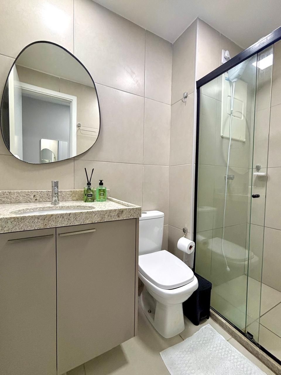A modern bathroom with a round mirror, a sink with toiletries, a toilet, and a glass-enclosed shower.