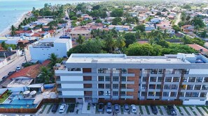 A multi-story hotel with a rooftop pool, surrounded by a coastal town with a beach and palm trees. - Maré Alta by AFT (Tamandaré)