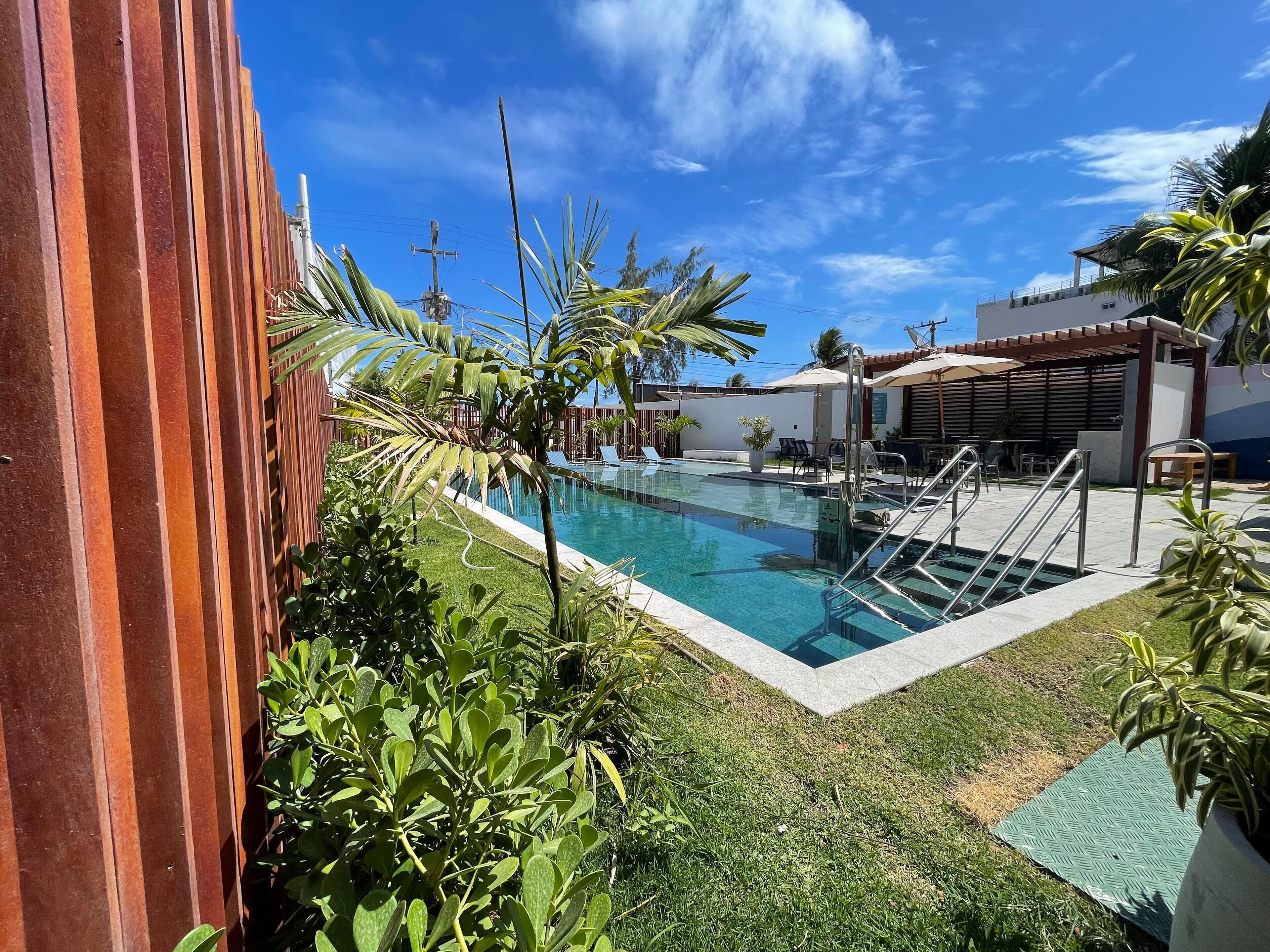 A swimming pool with a clear blue water, surrounded by a wooden fence, and a grassy area with a few potted plants.