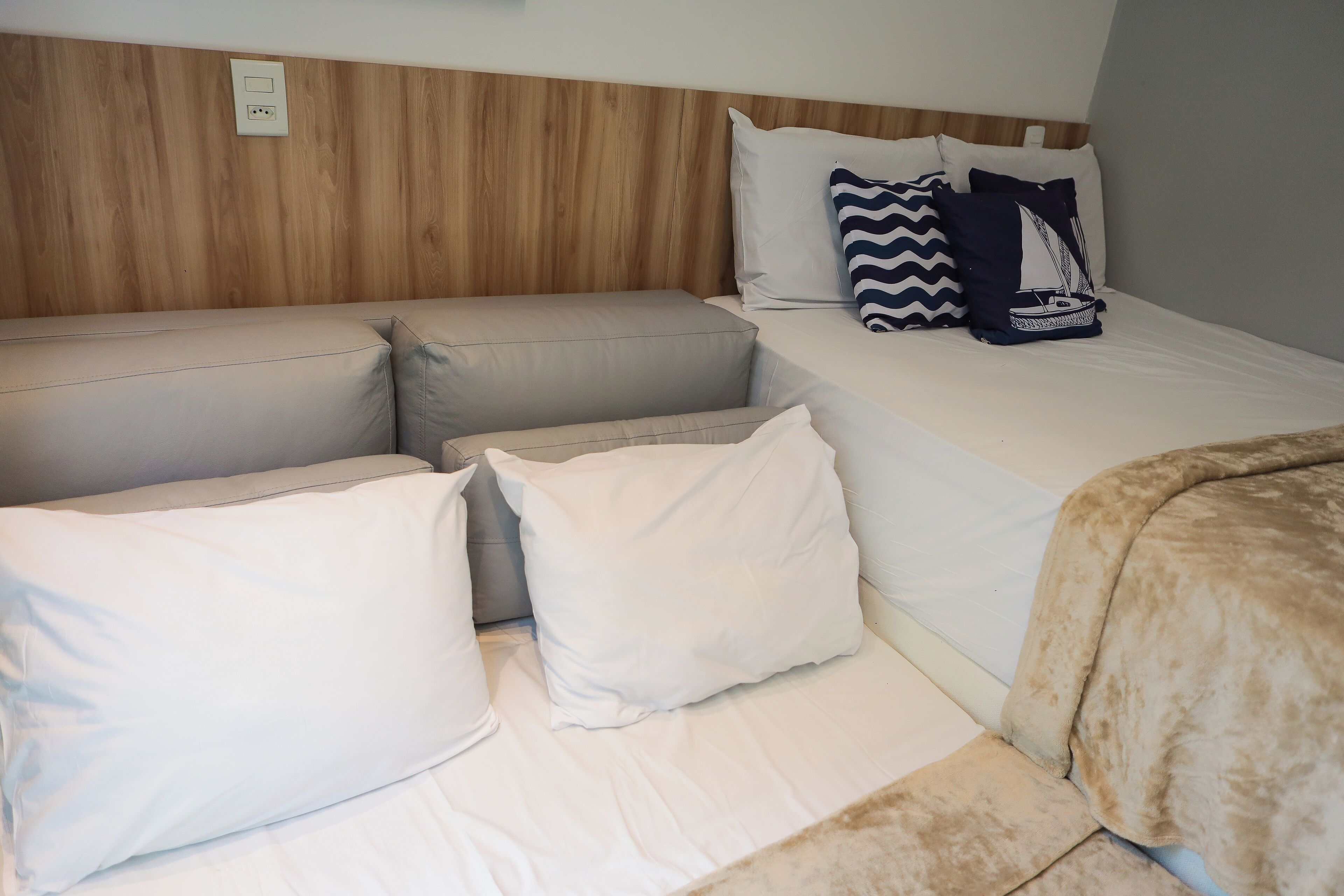 Een kamer met een bed, een slaapbank en een kleine zithoek. Er is een wand van houten panelen en een witte verdeeldoos.
