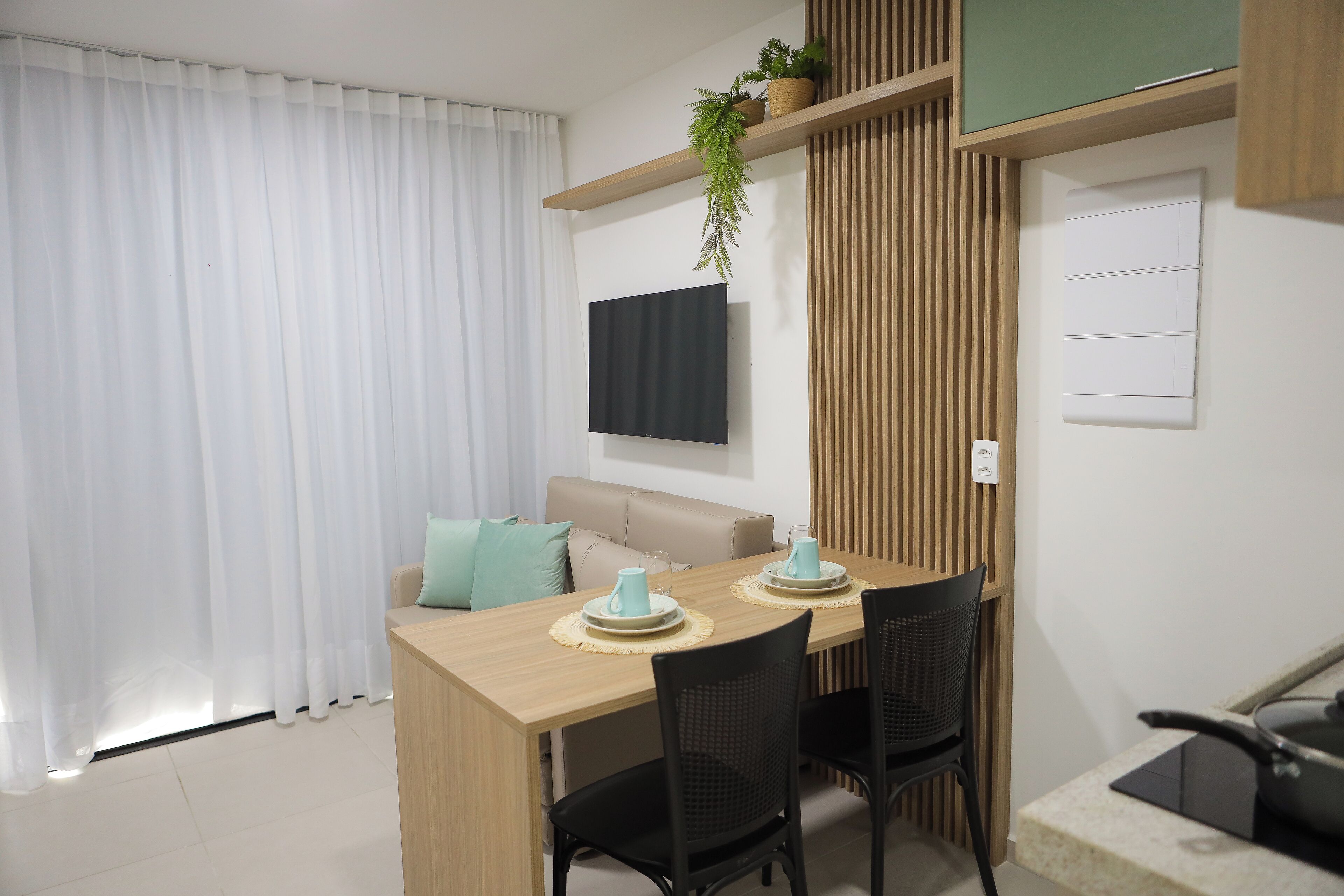 A modern dining area with a wooden table, black chairs, and a TV mounted on the wall.