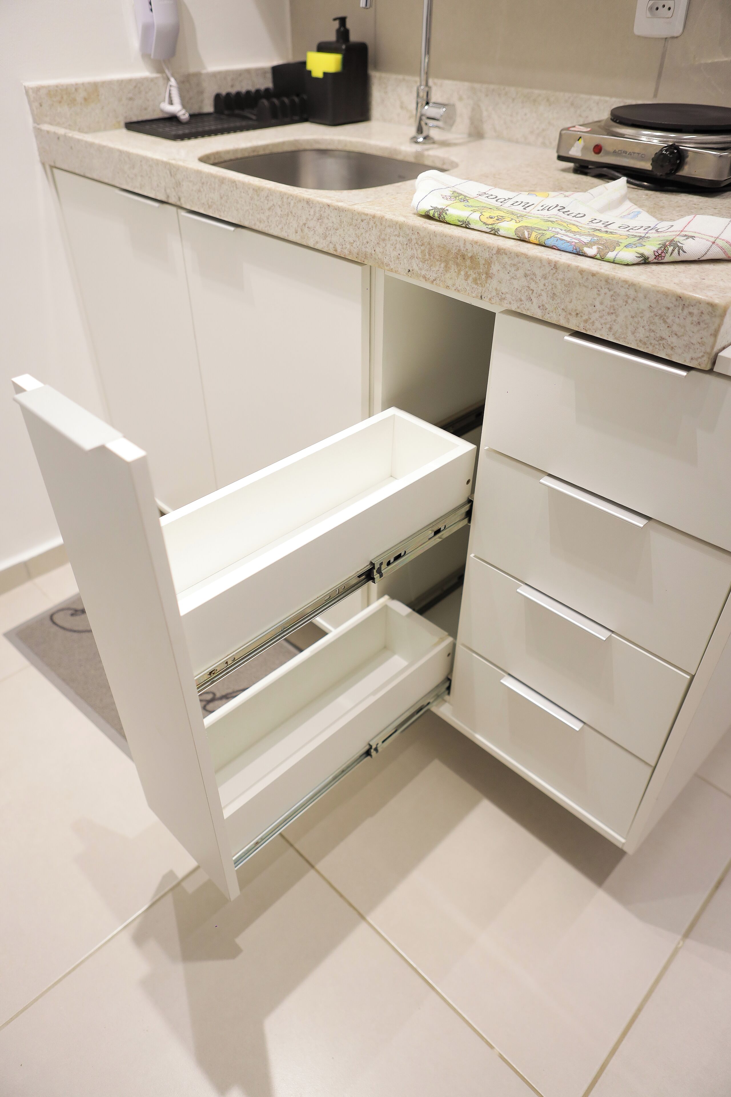 A kitchen with a stainless steel sink, a built-in oven, and a white cabinet with a drawer.