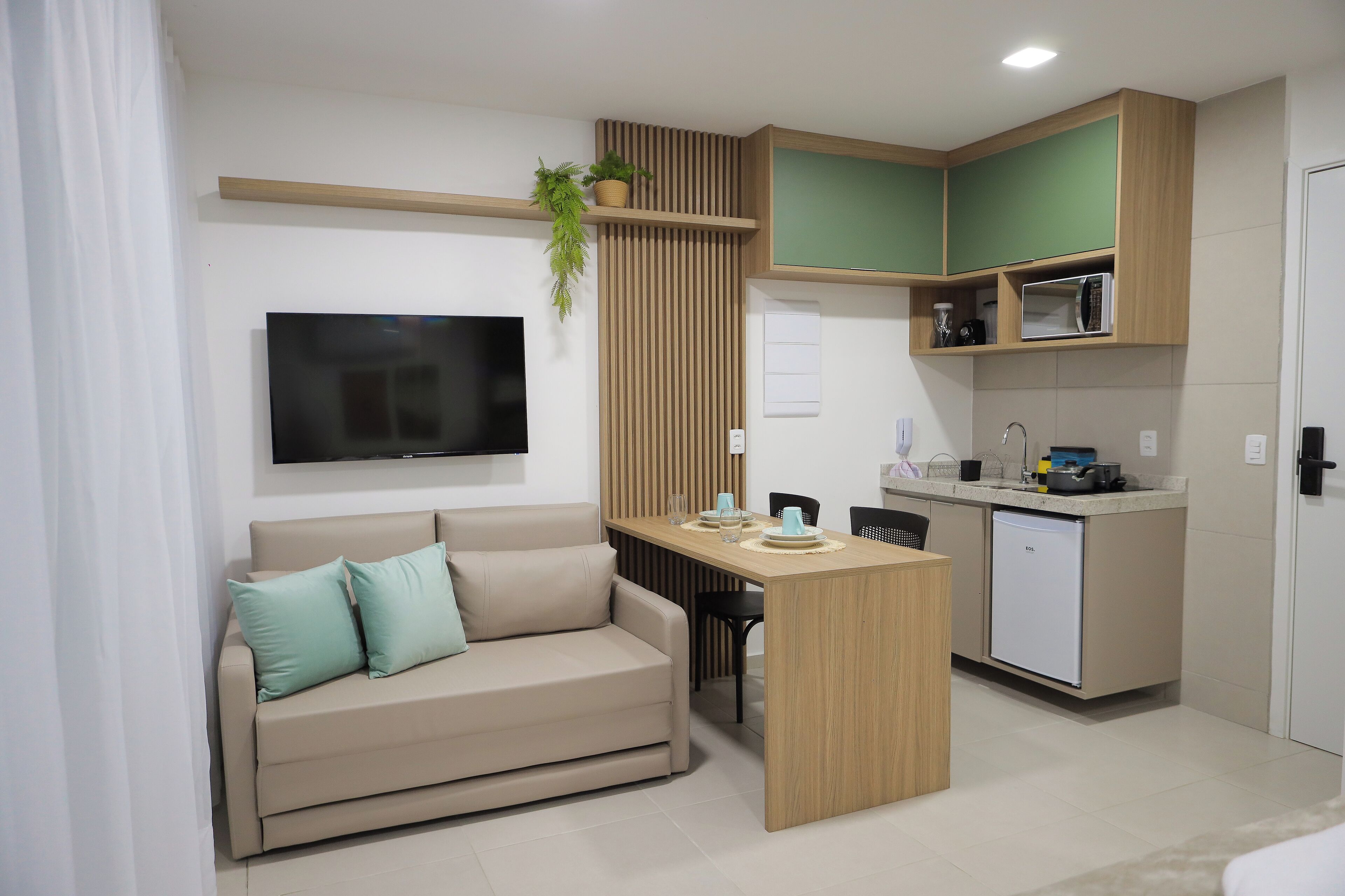 A compact living space with a sofa, a small kitchen area, and a TV mounted on the wall.