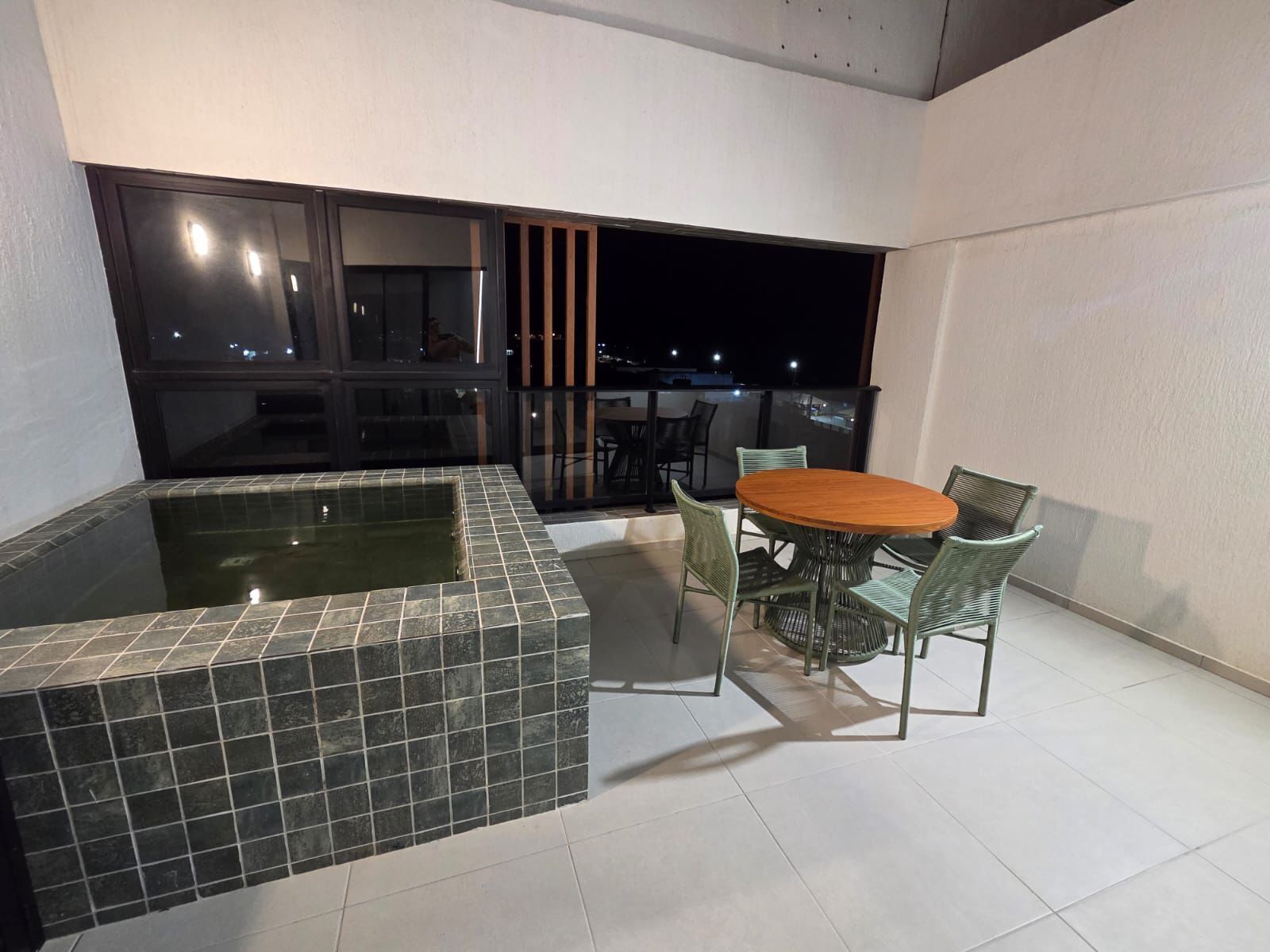 Un pequeño espacio al aire libre con un jacuzzi, una mesa redonda de madera y cuatro sillas.
