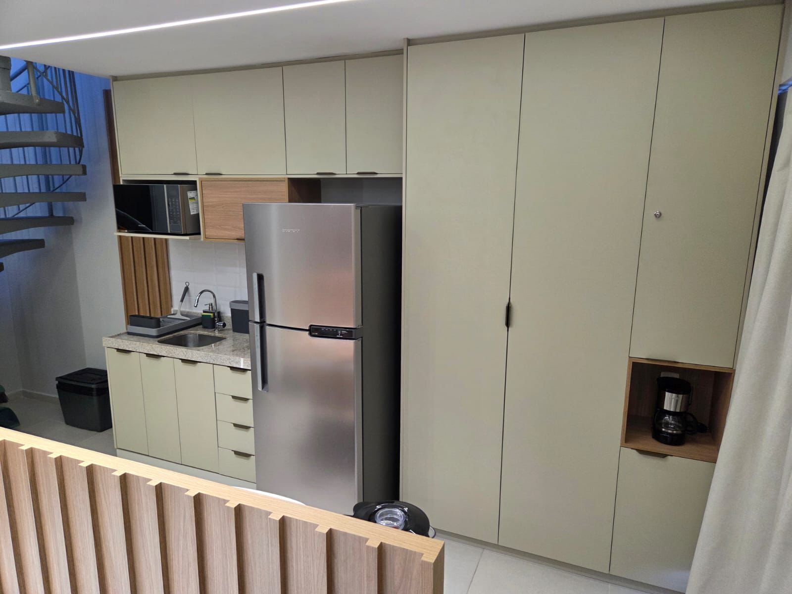 A modern kitchen with a built-in refrigerator, a microwave, and a coffee machine. There is a wooden counter and a sink.