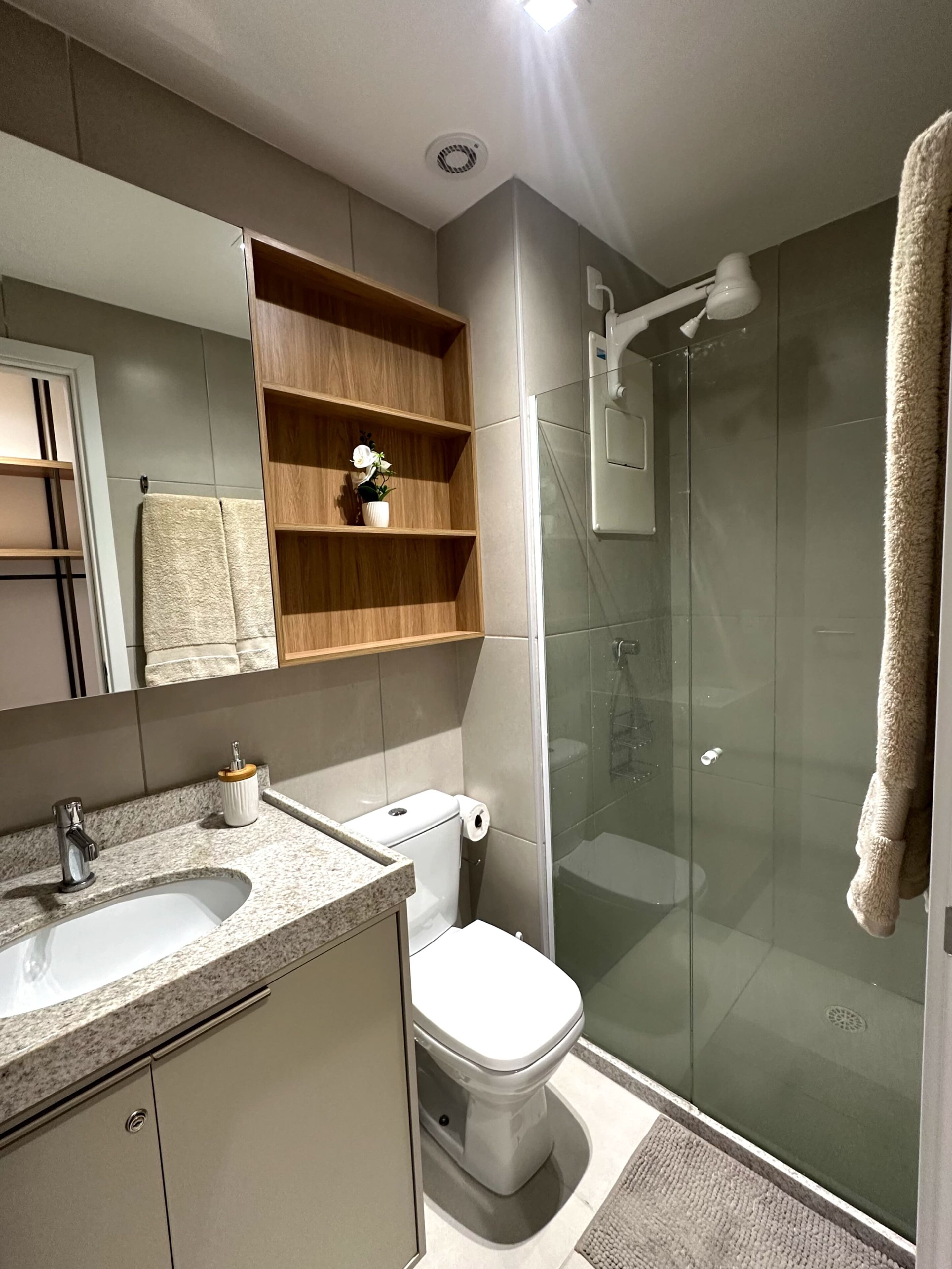 Ein modernes Badezimmer mit einer gläsernen Dusche, einem Waschtisch mit Spüle und Spiegel sowie einer Toilette mit Toilettenpapier.