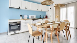 Une cuisine moderne avec des meubles blancs, un four à micro-ondes et un coin repas comprenant une table et des chaises en bois.