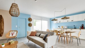 Un salon moderne avec un canapé, une table à manger et des chaises, une cuisine avec des meubles blancs et un mur d’accent bleu.