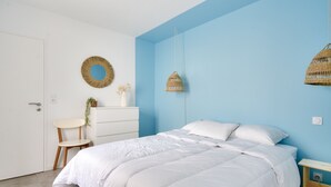 Une chambre à coucher comprenant un lit, une commode, une chaise, un miroir fixé au mur et un luminaire suspendu.