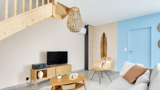 Un salon moderne avec un escalier en bois, un téléviseur à écran plat, un canapé, un fauteuil en osier et un mur d’accent bleu.