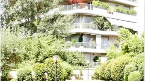 Un immeuble à plusieurs étages doté de balcons, entouré d’une végétation luxuriante.