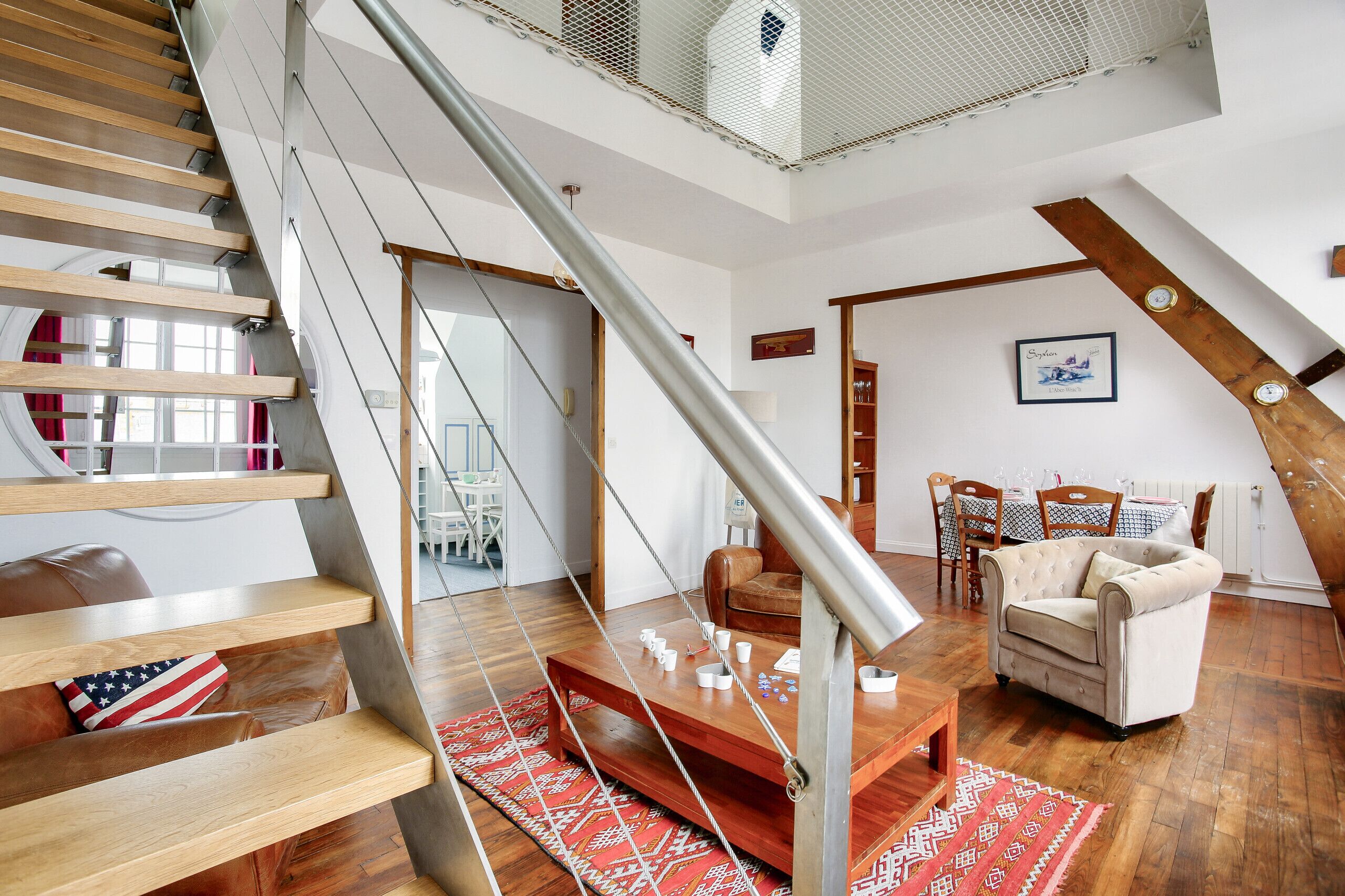Een ruime woonkamer met een houten trap, een eethoek en een gezellige zithoek.
