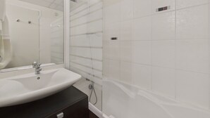 Un baño con lavamanos blanco, espejo y cabina de ducha con puerta de vidrio.