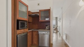Una cocina funcional con armarios de madera, microondas, lavavajillas y cafetera.