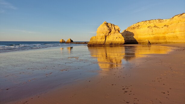 Une plage avec de grandes formations rocheuses et un ciel dégagé.