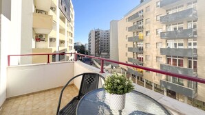 Un balcon avec une table ronde, un pot de fleurs et une rambarde rouge.
