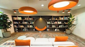 A modern library with a white sofa, orange cushions, and bookshelves filled with books. - Yas Island Waters Edge Studio (Abu Dhabi)
